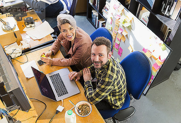 Portrait smiling  confident creative business people eating cereal  working at laptop in office