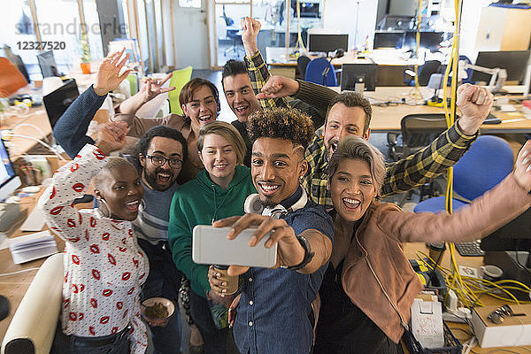 Enthusiastic creative business team cheering  taking selfie in office