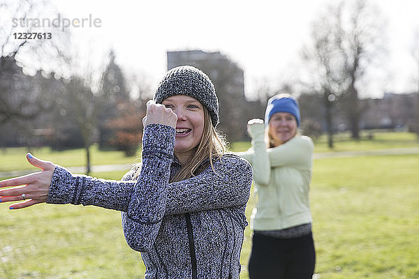 Smiling woman exercising  stretching arm in sunny park