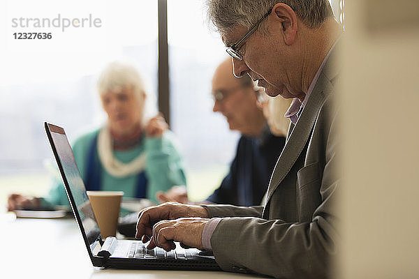 Focused senior businessman using laptop in conference room meeting