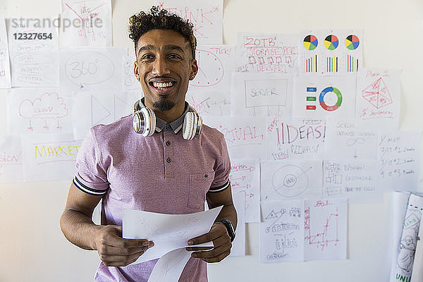 Portrait smiling  confident creative businessman hanging paperwork on office wall