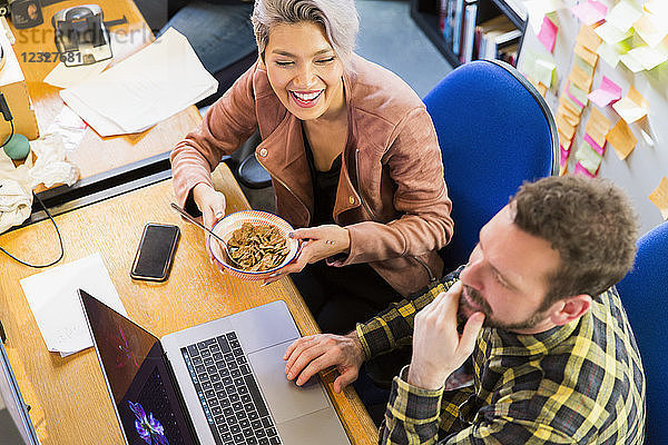 Creative business people eating cereal  working at laptop on office
