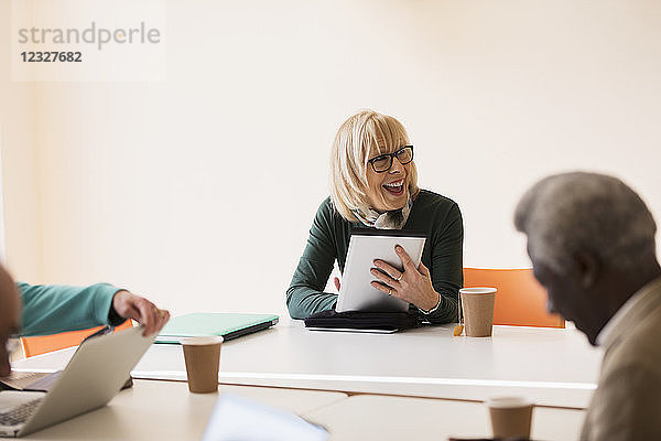 Smiling  confident senior businesswoman with digital tablet leading conference room meeting