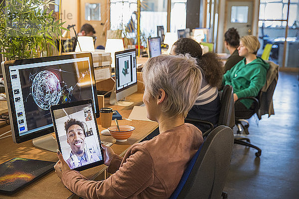 Creative businesswoman video chatting with businessman on digital tablet in open plan office