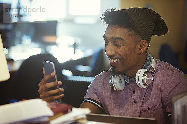 Smiling creative businessman texting with smart phone in office