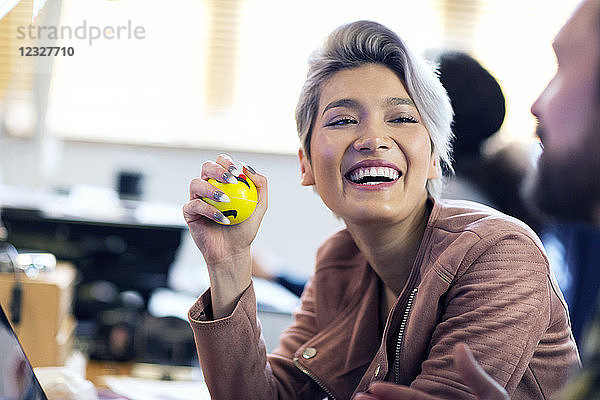 Laughing creative businesswoman squeezing stress ball in office