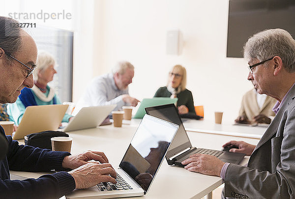 Senior businessmen using laptops in conference room meeting