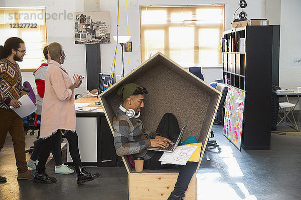 Creative businessman with headphones working at laptop in cubby