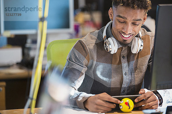 Creative businessman with headphones texting with smart phone at desk