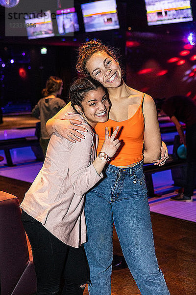 Portrait of smiling teenage girl showing peace sign while embracing friend at bowling alley