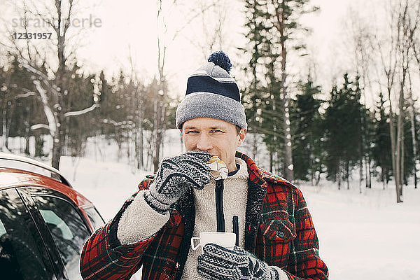Man eating bread while having coffee in car trunk at park during winter