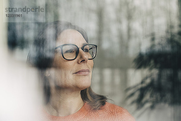 Close-up of thoughtful businesswoman wearing eyeglasses seen through window