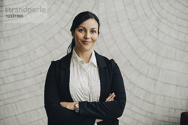 Portrait of businesswoman standing with arms crossed against wall at office