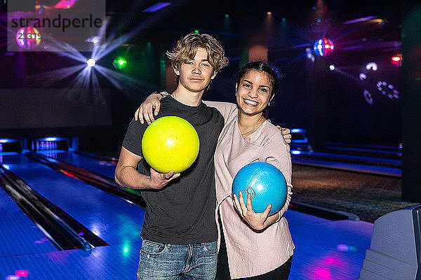 Portrait of smiling multi-ethnic teenage friends standing with balls at bowling alley