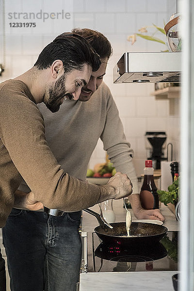 Smiling gay man standing with partner while pouring batter in cooking pan at kitchen