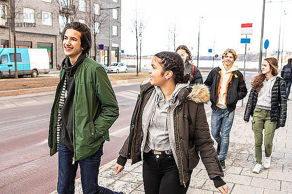 Smiling multi-ethnic teenagers wearing warm clothing walking on sidewalk in city