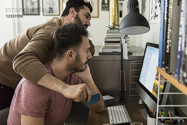 Gay couple shopping online through credit card on computer at home