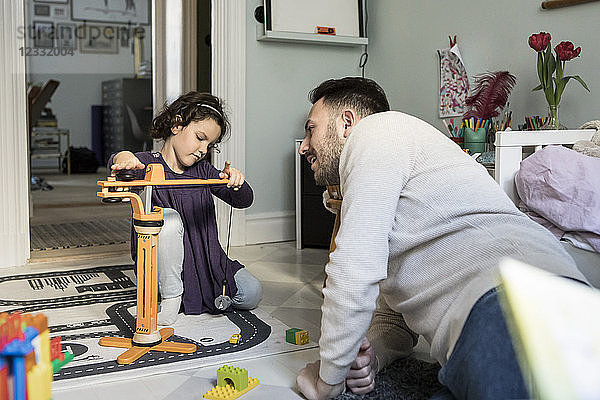 Father looking at daughter playing with crane toy in living room at home