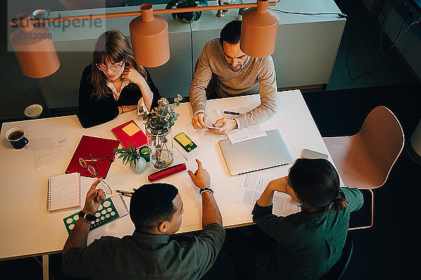 High angle view of multi-ethnic business team discussing while sitting at desk in creative office