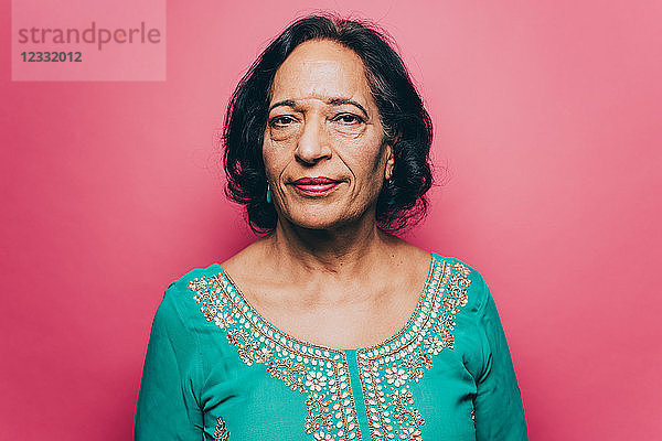 Portrait of confident senior woman with black short hair over pink background