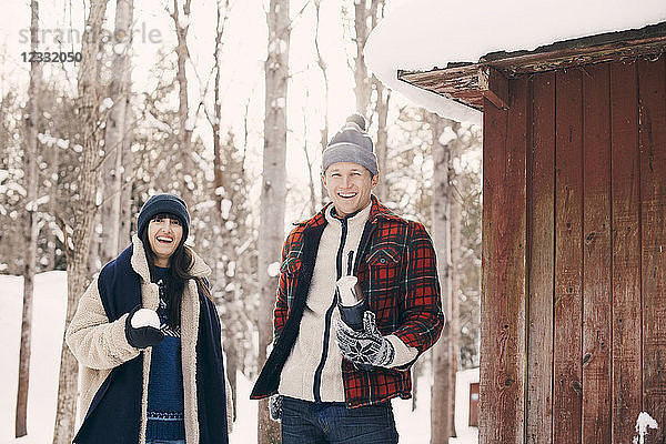 Portrait of happy friends holding snowball while standing by log cabin during winter