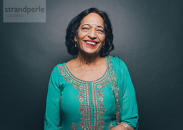 Portrait of smiling senior woman wearing salwar kameez against gray background