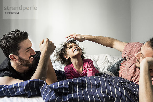 Fathers playing with cheerful daughter while lying on bed at home