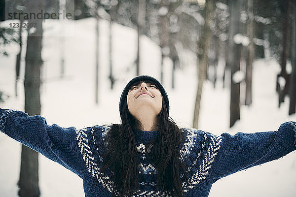 Happy woman standing with arms raised on snowy field during winter