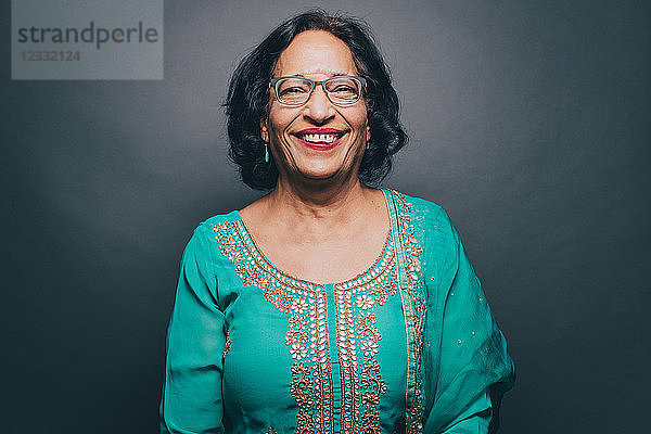 Portrait of smiling senior woman wearing salwar kameez on gray background