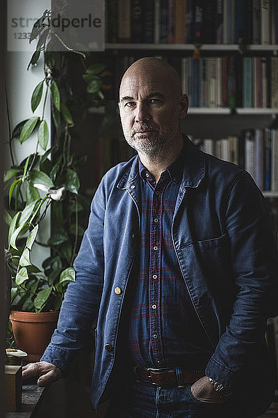 Portrait of confident mature therapist standing by potted plant at home office