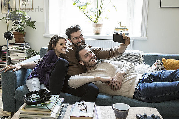 Fathers taking selfie with daughter through mobile phone on sofa at home