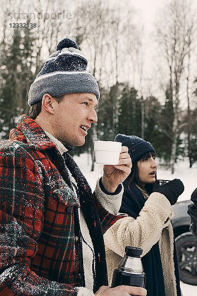 Smiling man standing with friend and having coffee during winter