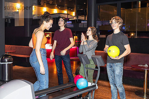 Happy teenage friends standing by rack at bowling alley