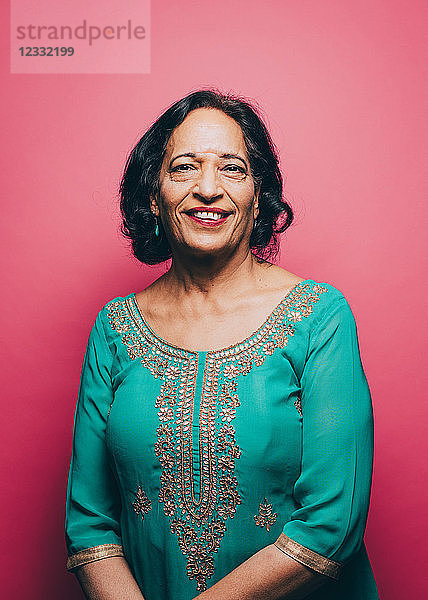 Portrait of smiling senior woman wearing salwar kameez against pink background