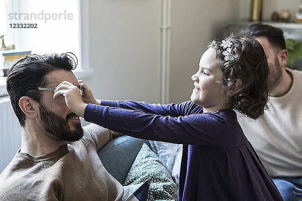 Daughter making father wear eyeglasses while sitting on sofa at home