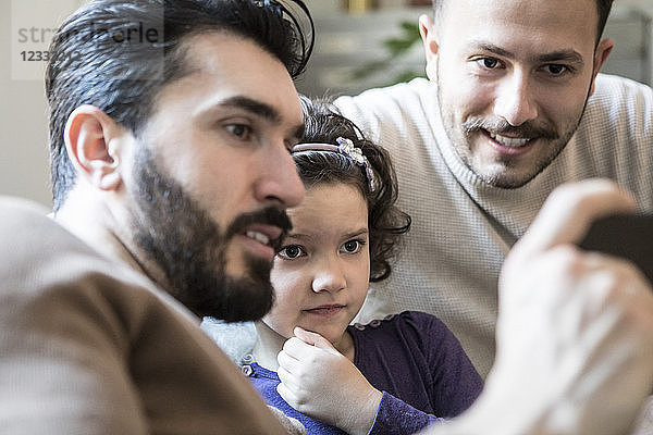 Fathers with curious daughter looking at smart phone while sitting at home