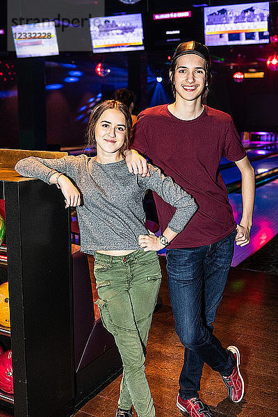 Portrait of smiling teenage friends standing by rack at bowling alley