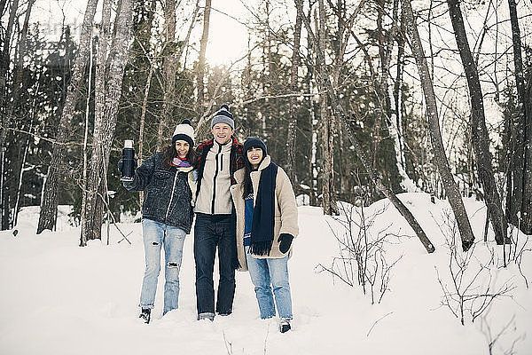Full length of smiling friends standing against trees on snow covered field