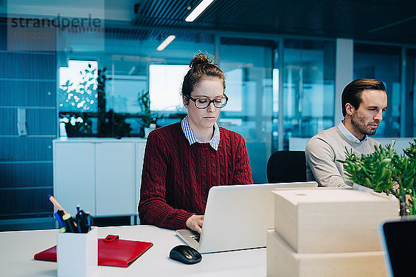 Businesswoman using laptop while sitting by colleague at desk in creative office