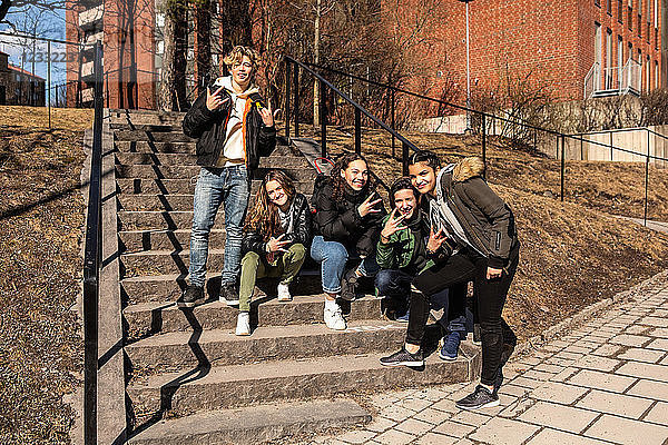 Portrait of cheerful multi-ethnic teenage friends showing hand signs on steps in city