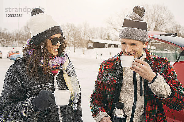 Smiling friends talking while having coffee at snowy park