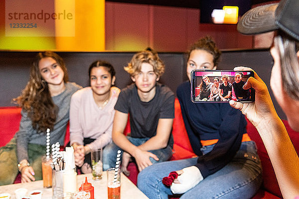 Cropped image of teenage boy photographing multi-ethnic friends sitting on sofa at restaurant