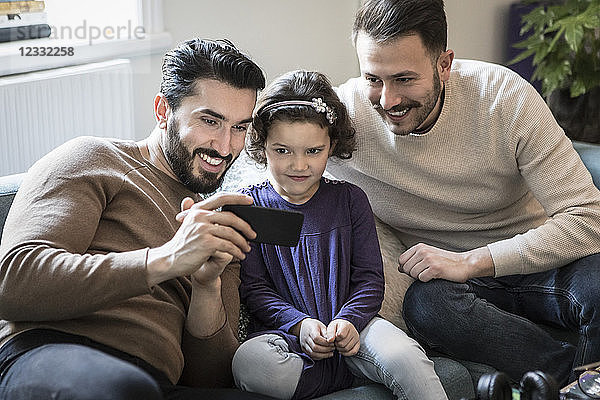 Fathers and daughter looking at smart phone while sitting on sofa at home