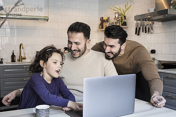 Happy fathers looking at daughter using laptop at table in kitchen