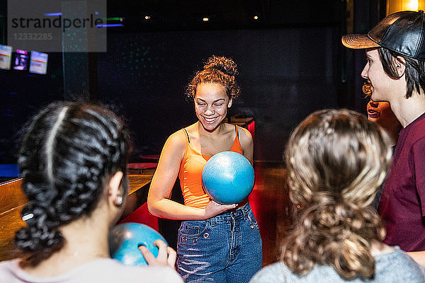 Smiling teenage girl holding bowling ball while standing amidst friends