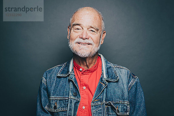 Portrait of smiling senior man wearing denim jacket against gray background