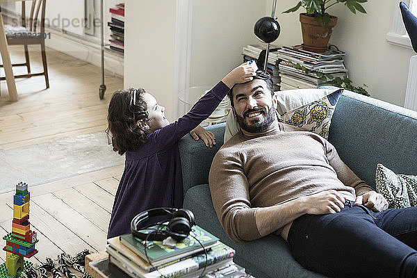 High angle view of girl keeping toy block on father's head lying on sofa at home