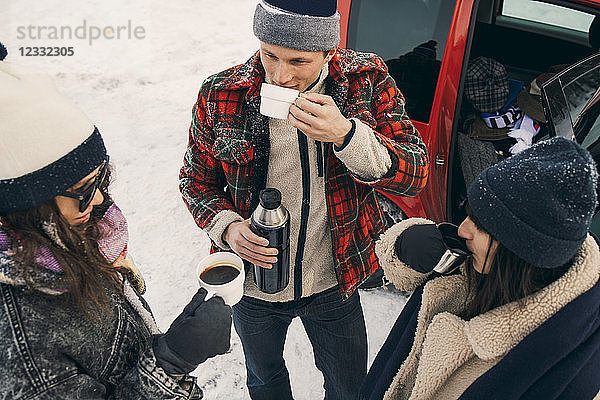 High angle view of friends having coffee while talking by car on snow