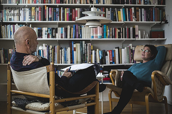 Male therapist discussing with female mature patient against bookshelf at home office