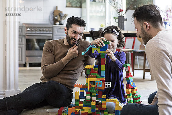 Gay parents looking at daughter playing with blocks at home